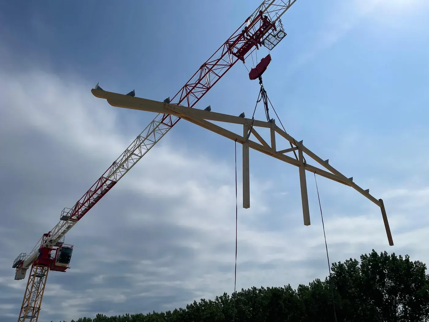 Ferme de charpente en lamellé-collé suspendue à la grue au-dessus du chantier