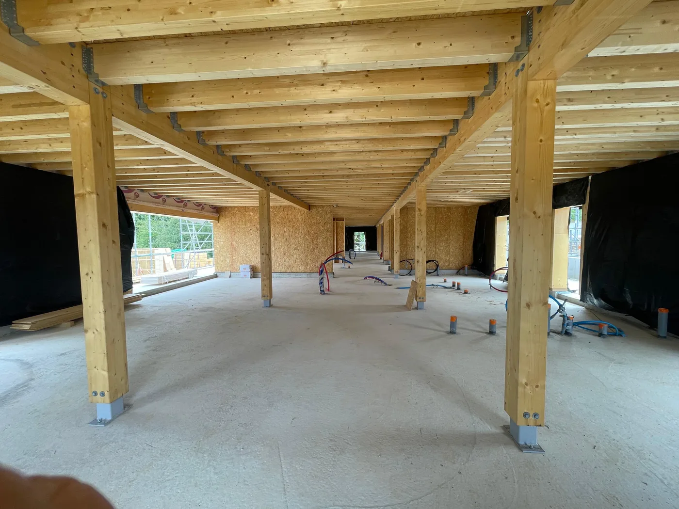 Intérieur du bâtiment bois-paille : poteaux et solivage en bois apparents sur la dalle
