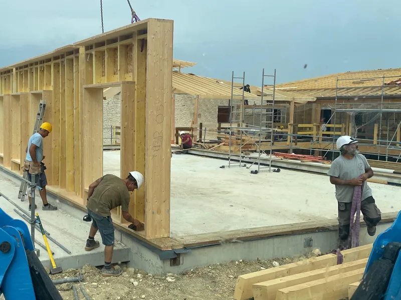 Pose d'un mur à ossature bois levé à la grue, l'équipe ACMT au calage sur la dalle