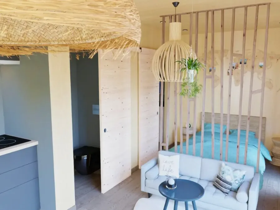 Intérieur d'un studio en ossature bois : coin cuisine, espace nuit séparé par un claustra, lumière naturelle
